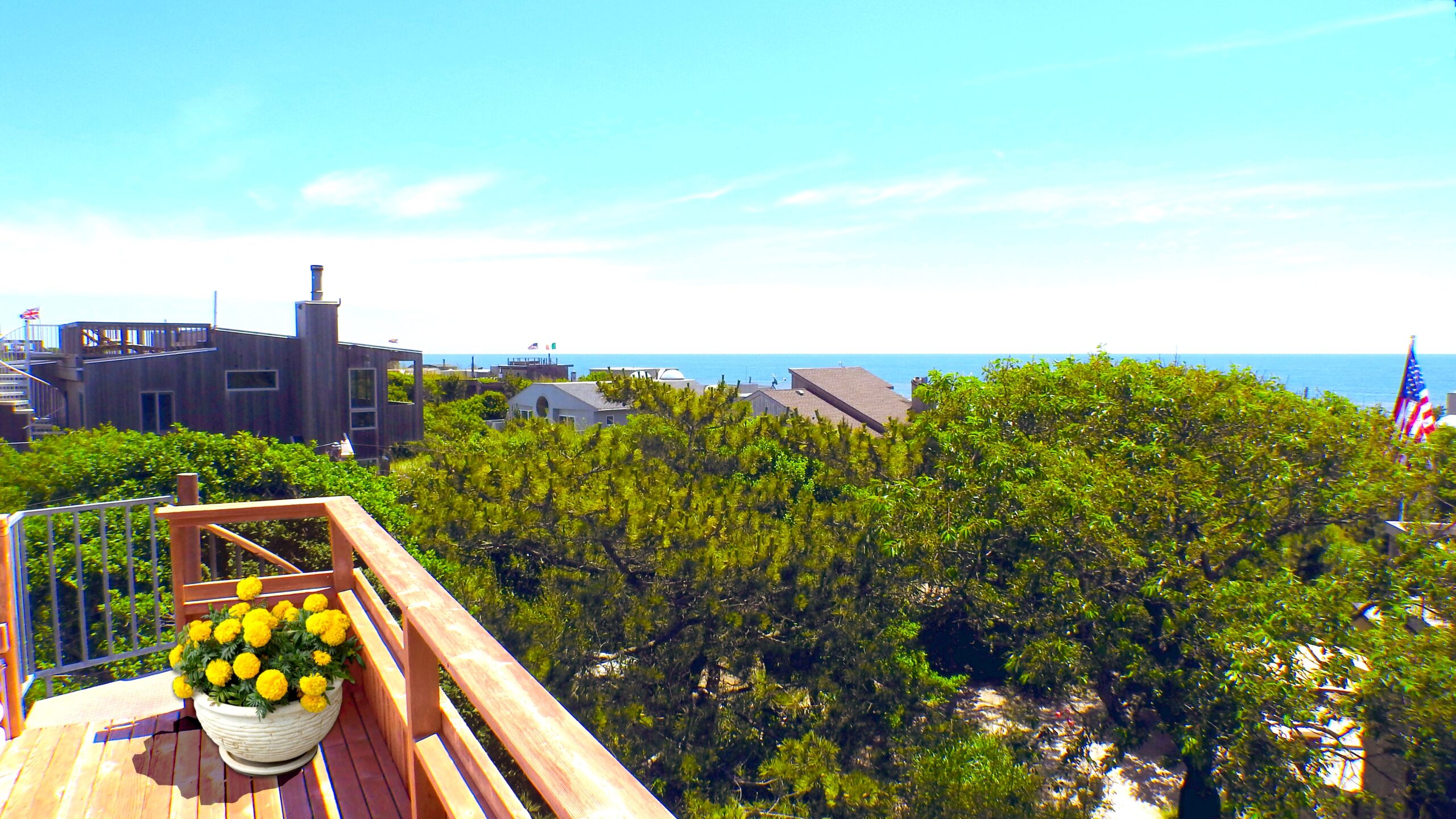 View from high up deck overlooking the Atlantic Ocean along the Fire Island Pines coast with view of trees, the deep blue ocean and the sunny blue sky.